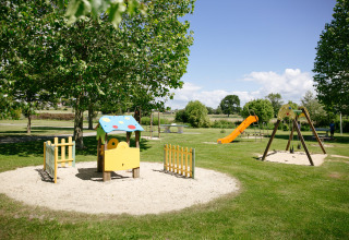 Speeltuin met schommels, glijbaan en speelhuisje in het gras bij Camping Seasonova Saint Michel, Normandië.