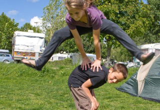 Due bambini giocano a salto della cavallina sull’erba al Camping Seasonova Saint Michel in Normandia, Francia.
