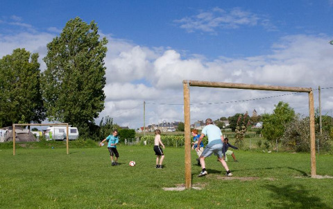 Niños y adultos juegan al fútbol en un campo verde en el camping Seasonova Saint Michel en Normandía, Francia.