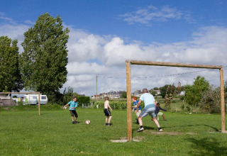 Kinderen en volwassenen spelen voetbal op het grasveld bij Camping Seasonova Saint Michel in Normandië, Frankrijk.