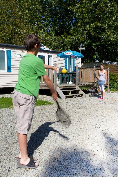 Zwei Kinder spielen Badminton außerhalb eines Mobilheims im Camping Seasonova Saint Michel, Normandie.