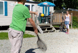 Twee kinderen spelen badminton buiten een caravan op Camping Seasonova Saint Michel in Normandië, Frankrijk.