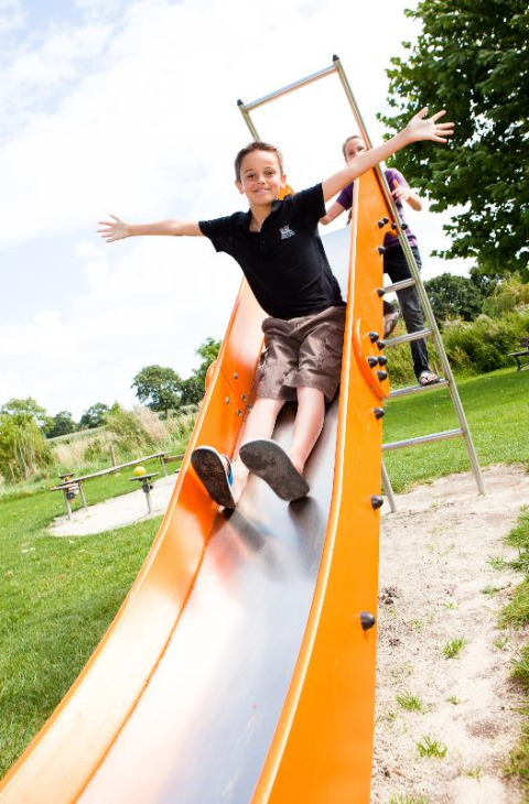Ragazzo che scivola felicemente su uno scivolo arancione a Camping Seasonova Saint Michel, Normandia, Francia.