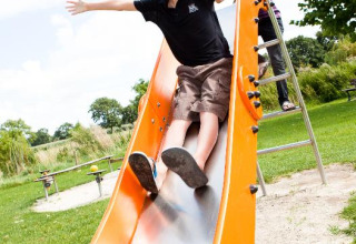 Jongen glijdt blij van een oranje glijbaan op Camping Seasonova Saint Michel, Normandië, Frankrijk.