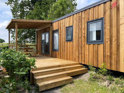 Esterno del Prestige Cottage lodge con rivestimento in legno, terrazza e tavolo da picnic sotto una pergola.