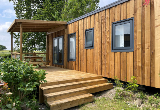 Esterno del Prestige Cottage lodge con rivestimento in legno, terrazza e tavolo da picnic sotto una pergola.