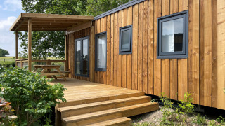 Esterno del Prestige Cottage lodge con rivestimento in legno, terrazza e tavolo da picnic sotto una pergola.