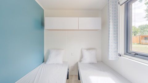 Lyst værelse i Prestige Cottage med to enkeltsenge, skabe, blå væg og stort vindue med udsigt.