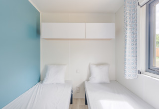 Lyst værelse i Prestige Cottage med to enkeltsenge, skabe, blå væg og stort vindue med udsigt.