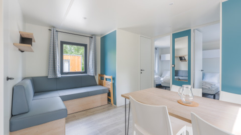 Licht lodge-interieur met moderne meubels, hoekbank, eettafel, stoelen en zicht op een slaapkamer.