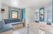 Lyst lodgeinteriør med moderne møbler, sofa, spisebord, stole og soveværelse i baggrunden.