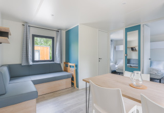 Licht lodge-interieur met moderne meubels, hoekbank, eettafel, stoelen en zicht op een slaapkamer.