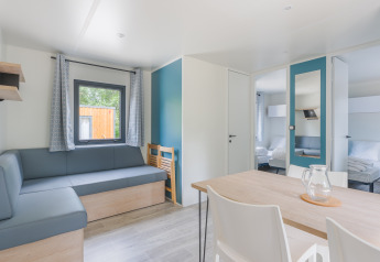 Lyst lodgeinteriør med moderne møbler, sofa, spisebord, stole og soveværelse i baggrunden.