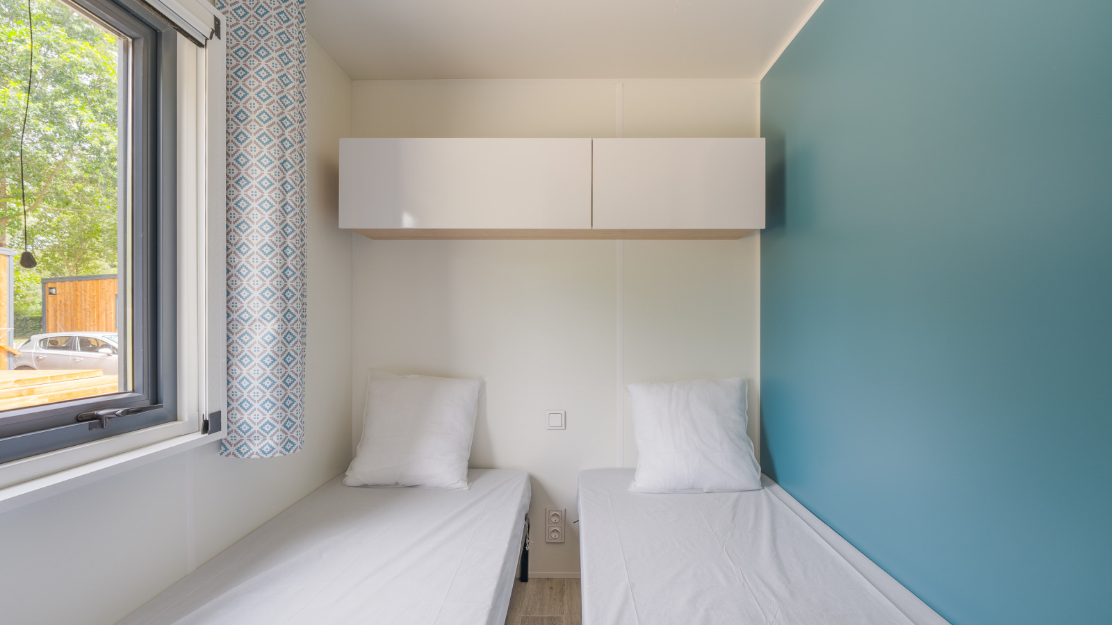 Twee eenpersoonsbedden met wit beddengoed in een lichte kamer met blauwe muur in Prestige Cottage, Frankrijk.