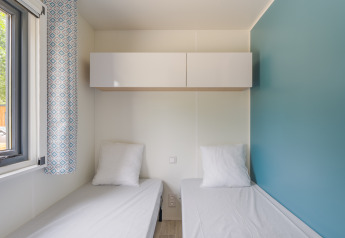 Two single beds with white linen in a bright room with blue accent wall at Prestige Cottage, Camping Seasonova, France.