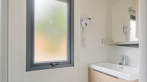 Baño moderno de lodge con ventana esmerilada, lavabo, espejo y secador de pelo en la pared.