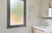 Baño moderno de lodge con ventana esmerilada, lavabo, espejo y secador de pelo en la pared.