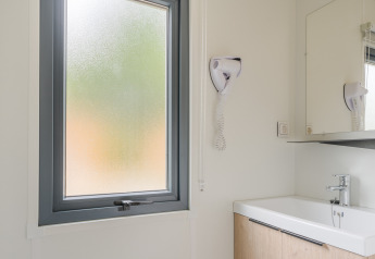 Moderne lodgebadkamer met matglasraam, wastafel, spiegel en wandgemonteerde föhn zichtbaar.