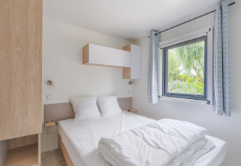 Dormitorio moderno del lodge Prestige Cottage con cama doble, ventana, cortinas azules y decoración sencilla.
