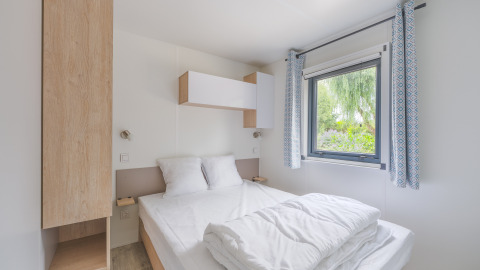 Chambre moderne d’un lodge Prestige Cottage avec lit double, fenêtre, rideaux bleus et décoration épurée.