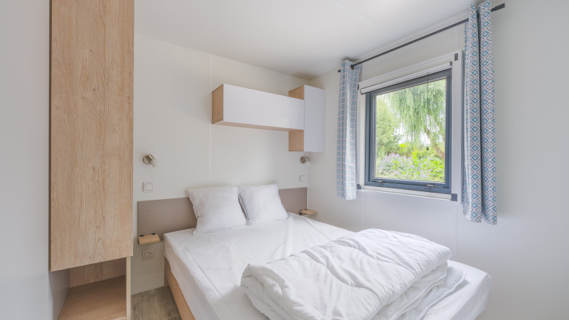 Moderne slaapkamer in Prestige Cottage lodge met tweepersoonsbed, raam, blauwe gordijnen en eenvoudig decor.