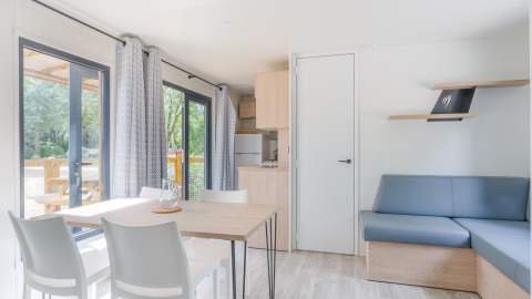 Luminoso e moderno lodge Prestige Cottage con tavolo da pranzo, divano, cucina e ampie finestre sulla natura.