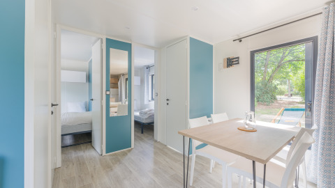 Bright and modern Prestige Cottage lodge interior with dining table, chairs, bedrooms, and outdoor view.