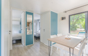 Licht, modern interieur in Prestige Cottage lodge met eettafel, stoelen, slaapkamers en tuinzicht.