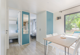 Bright and modern Prestige Cottage lodge interior with dining table, chairs, bedrooms, and outdoor view.
