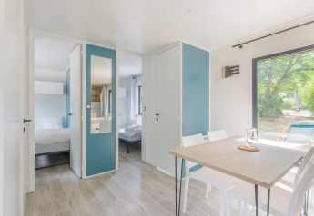 Bright and modern Prestige Cottage lodge interior with dining table, chairs, bedrooms, and outdoor view.