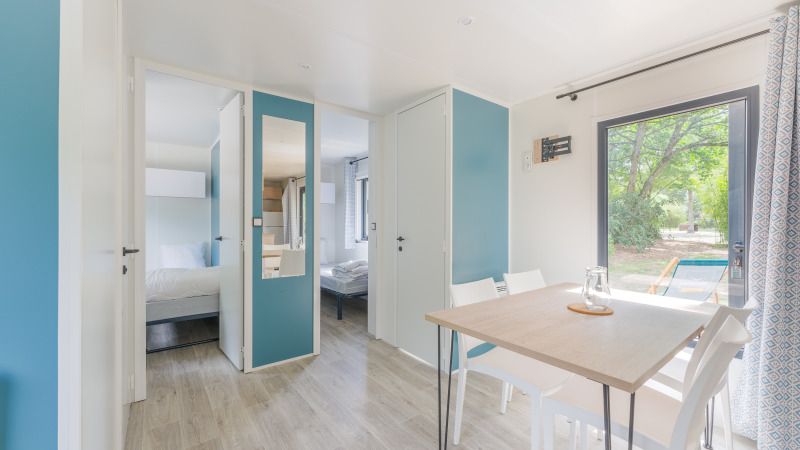 Licht en modern interieur van Prestige Cottage lodge met eettafel, stoelen, slaapkamers en buitenzicht.