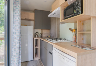 Cocina moderna en Prestige Cottage con estufa, microondas, nevera y vista al exterior verde.