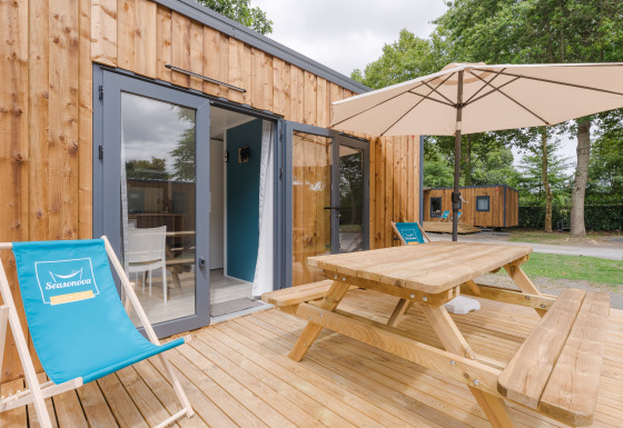 Udendørs terrasse ved Prestige Cottage med træmøbler, parasol og liggestole foran indgangsdøren.