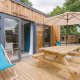 Udendørs terrasse ved Prestige Cottage med træmøbler, parasol og liggestole foran indgangsdøren.