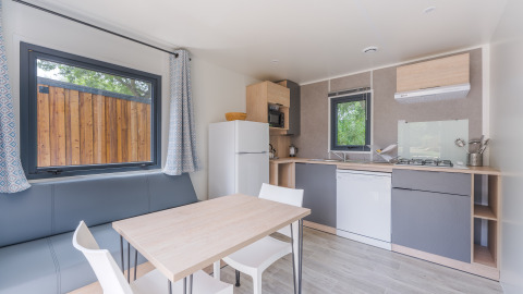 Modern glamping accommodation with a fully equipped kitchen, dining table, large windows, and sofa.