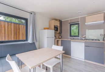 Moderne glamping-accommodatie met uitgeruste keuken, eettafel, grote ramen en grijze zetel.