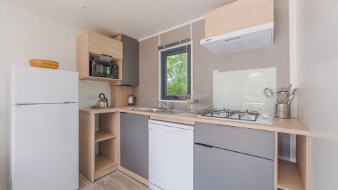 Modern glamping kitchen with fridge, gas stove, dishwasher, microwave, and a window with a nature view.