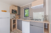 Moderne glampkeuken met koelkast, gasvuur, vaatwasser, microgolfoven en raam met zicht op natuur.