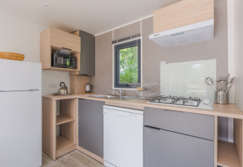 Cucina glamping moderna con frigorifero, fornello a gas, lavastoviglie, microonde e finestra panoramica.