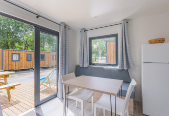 Interior de una cabaña moderna con mesa de comedor, sillas, nevera y vista a terraza de madera y otras cabañas.