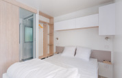 Lichte, moderne glampingaccommodatie met tweepersoonsbed, open kast en eigen badkamer.