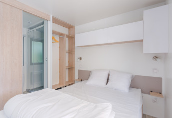 Lichte, moderne glampingaccommodatie met tweepersoonsbed, open kast en eigen badkamer.