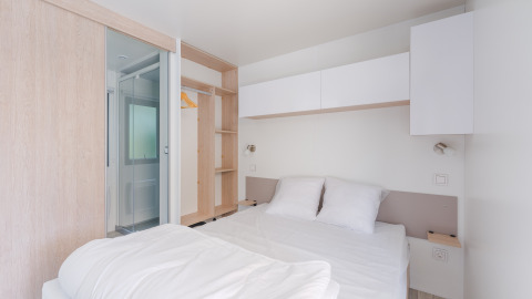 Helles, modernes Glamping-Zimmer mit Doppelbett, Stauraum, Hängeschrank und Bad mit Glastür.