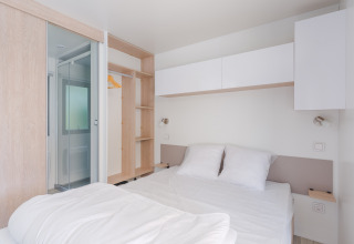 Luminoso alojamiento glamping moderno con cama doble, armario abierto y baño integrado.