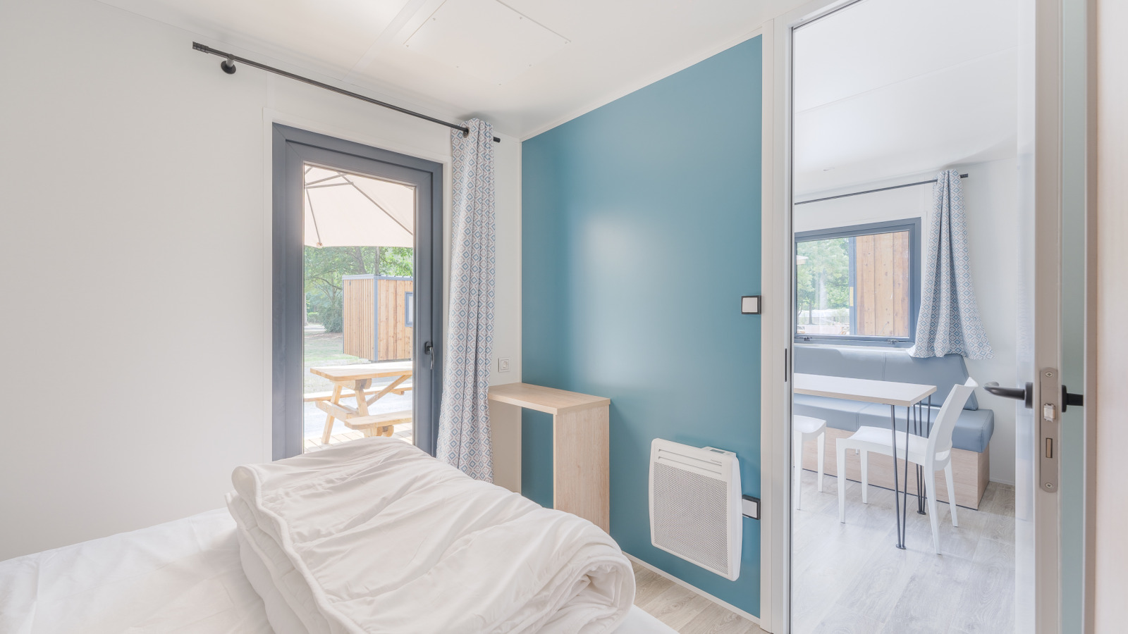 Lichte moderne lodgekamer met zicht op kleine eethoek en buiten terras met picknicktafel.