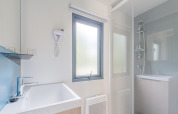 Helles, modernes Badezimmer in einer Glamping-Unterkunft mit Dusche, Fenster, Waschbecken und Föhn.