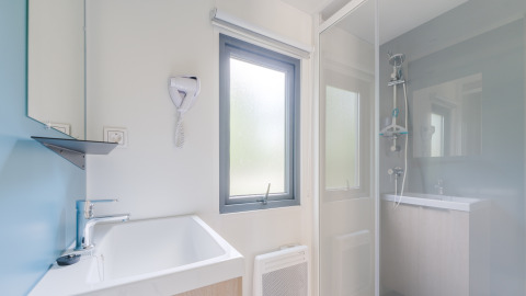 Bagno moderno e luminoso in una struttura glamping con doccia, finestra, lavandino e asciugacapelli a muro.