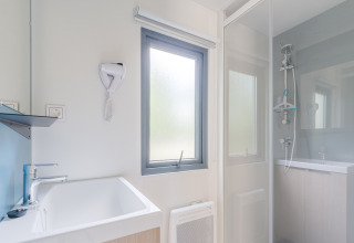 Bagno moderno e luminoso in una struttura glamping con doccia, finestra, lavandino e asciugacapelli a muro.