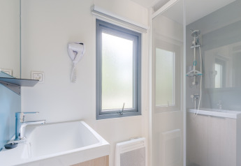 Baño moderno y luminoso en alojamiento glamping, con ducha, ventana, lavabo y secador de pelo de pared.