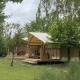 Safari-telte ved Slow Lodge omgivet af grønne træer og græs, ideelle til afslappende udendørs ophold.